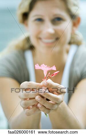 Stock Image - Woman holding flower in hands, smiling at camera, focus on foreground. Fotosearch