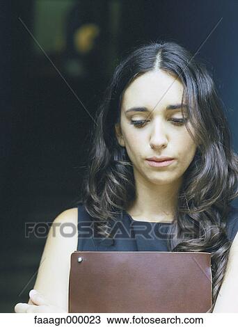 Woman holding folder in front of chest, looking down View Large Photo Image Stock Image - Woman holding folder in front of chest, looking down. Fotosearch
