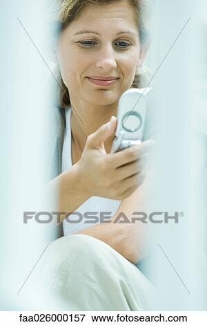 Stock Photo - Woman holding up cell phone, smiling, selective focus. Fotosearch