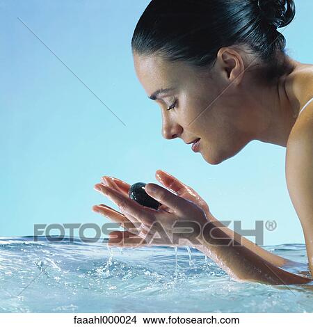 Picture - Woman in water holding stones in hands with eyes closed, side view. Fotosearch