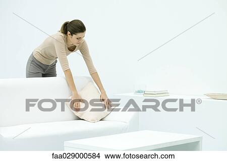 Picture - Woman leaning over couch, arranging pillow. Fotosearch
