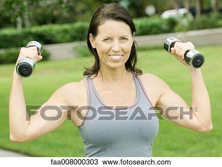 Woman lifting weights outdoors, smiling View Large Photo Image Stock Image - Woman lifting weights outdoors, smiling. Fotosearch