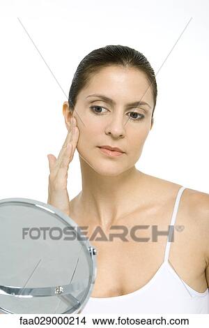 Picture - Woman looking at herself in mirror, touching cheek. Fotosearch