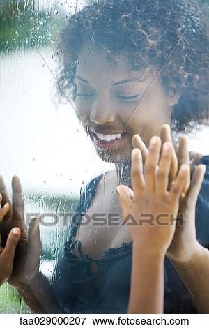 Woman looking through window, holding her hands up to child's hands through glass View Large Photo Image Stock Photo - Woman looking through window, holding her hands up to child's hands through glass. Fotosearch