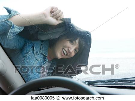 Stock Image - Woman looking through windshield, holding jacket over head. Fotosearch