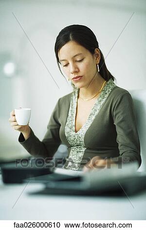 Woman sitting at desk, holding coffee cup, looking down View Large Photo Image Stock Image - Woman sitting at desk, holding coffee cup, looking down. Fotosearch