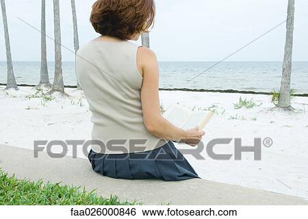 Woman sitting at the beach reading book, rear view View Large Photo Image Stock Photograph - Woman sitting at the beach reading book, rear view. Fotosearch