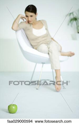 Picture - Woman sitting in chair, looking at apple in the floor in foreground. Fotosearch