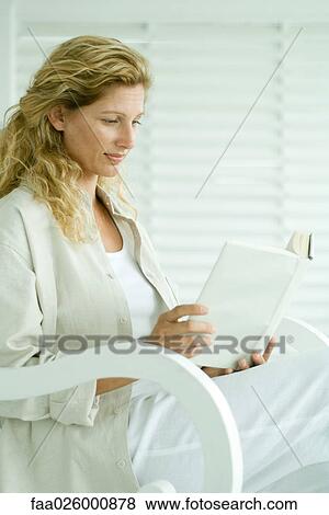Stock Photo - Woman sitting in rocking chair, reading book, smiling. Fotosearch