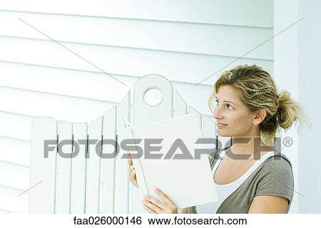 Woman sitting on bench, holding book, looking away View Large Photo Image Stock Photograph - Woman sitting on bench, holding book, looking away. Fotosearch