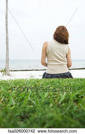 Woman sitting on ground, facing sea, rear view View Large Photo Image Stock Image - Woman sitting on ground, facing sea, rear view. Fotosearch