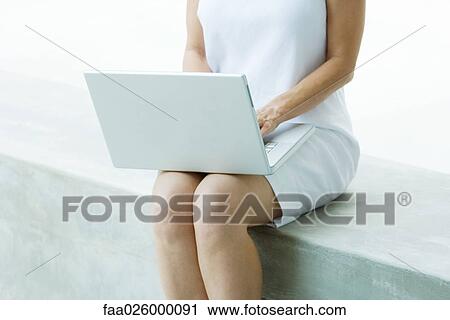 Woman sitting on low wall, using laptop computer, cropped view View Large Photo Image Stock Image - Woman sitting on low wall, using laptop computer, cropped view. Fotosearch