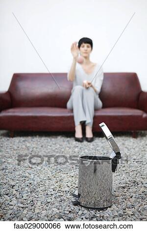 Woman sitting on sofa, throwing ball at garbage can in foreground View Large Photo Image Stock Photograph - Woman sitting on sofa, throwing ball at garbage can in foreground. Fotosearch
