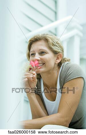 Woman sitting outdoors, smelling flower, looking away View Large Photo Image Stock Photo - Woman sitting outdoors, smelling flower, looking away. Fotosearch