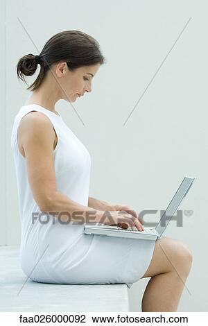 Woman sitting, using laptop computer, side view View Large Photo Image Stock Image - Woman sitting, using laptop computer, side view. Fotosearch