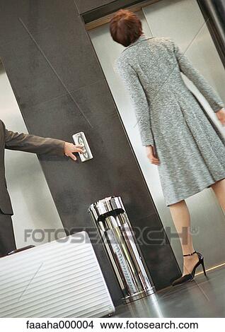 Picture - Woman standing in front of elevator, man pushing button. Fotosearch