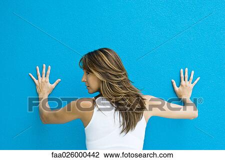 Woman standing with hands against blue wall, looking over shoulder, rear view View Large Photo Image Stock Image - Woman standing with hands against blue wall, looking over shoulder, rear view. Fotosearch