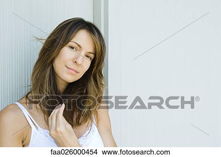 Woman touching her hair, head tilted, smiling at camera View Large Photo Image Picture - Woman touching her hair, head tilted, smiling at camera. Fotosearch