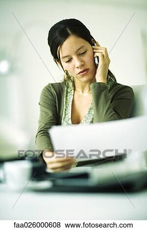 Stock Photo - Woman using cell phone, looking down at document, selective focus. Fotosearch