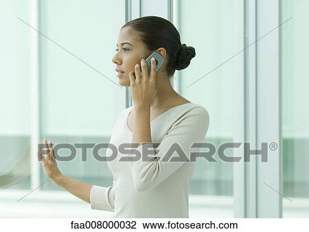 Stock Image - Woman using cell phone next to window. Fotosearch