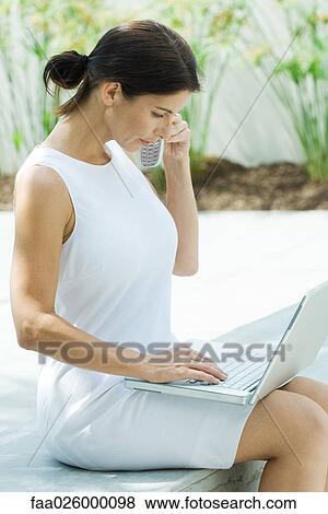 Woman using cell phone outdoors, looking down at laptop computer View Large Photo Image Stock Photo - Woman using cell phone outdoors, looking down at laptop computer. Fotosearch