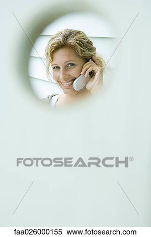 Woman using cell phone, smiling at camera, viewed through hole View Large Photo Image Stock Photography - Woman using cell phone, smiling at camera, viewed through hole. Fotosearch