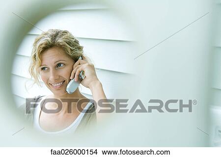 Woman using cell phone, smiling, viewed through hole View Large Photo Image Picture - Woman using cell phone, smiling, viewed through hole. Fotosearch