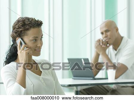 Stock Image - Woman using cell phone while man watches her in background. Fotosearch
