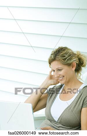 Woman using laptop computer, smiling, looking down View Large Photo Image Stock Photo - Woman using laptop computer, smiling, looking down. Fotosearch