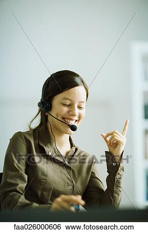 Woman wearing headset, index finger raised, smiling, looking down View Large Photo Image Stock Photograph - Woman wearing headset, index finger raised, smiling, looking down. Fotosearch