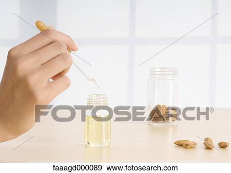 Stock Photo - Woman's hand holding dropper of essential oil with almonds. Fotosearch