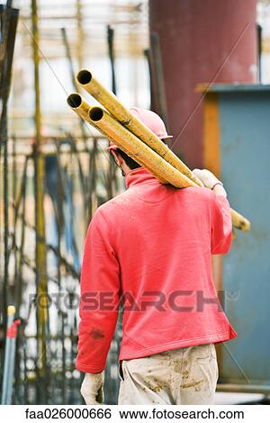 Worker at construction site carrying metal rods on shoulder View Large Photo Image Stock Photograph - Worker at construction site carrying metal rods on shoulder. Fotosearch