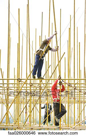 Stock Photograph - Workers assembling metal scaffolding at construction site. Fotosearch