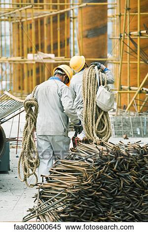 Workers at construction site carrying rope, metal rods stacked in foreground View Large Photo Image Stock Photography - Workers at construction site carrying rope, metal rods stacked in foreground. Fotosearch