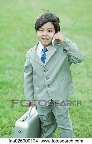 Young boy dressed in suit, holding up cell phone, carrying briefcase View Large Photo Image Picture - Young boy dressed in suit, holding up cell phone, carrying briefcase. Fotosearch