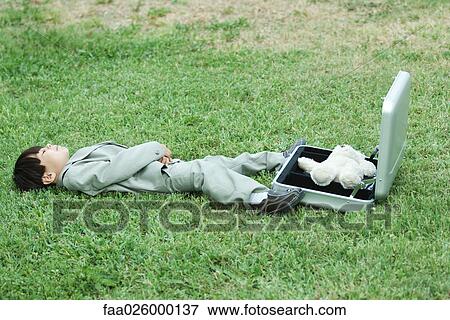 Young boy dressed in suit, lying in grass next to open briefcase containing teddy bear View Large Photo Image Stock Photo - Young boy dressed in suit, lying in grass next to open briefcase containing teddy bear. Fotosearch