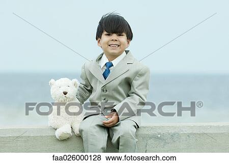 Young boy dressed in suit, sitting on ledge next to teddy bear, smiling at camera View Large Photo Image Stock Photo - Young boy dressed in suit, sitting on ledge next to teddy bear, smiling at camera. Fotosearch