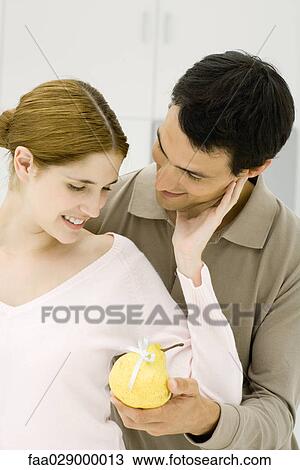 Young couple in kitchen, man handing woman a pear with a bow on it View Large Photo Image Stock Image - Young couple in kitchen, man handing woman a pear with a bow on it. Fotosearch