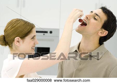 Young couple in kitchen, woman feeding man cherry View Large Photo Image Stock Photo - Young couple in kitchen, woman feeding man cherry. Fotosearch