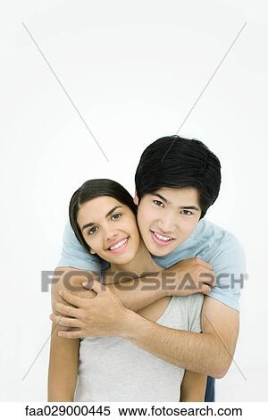 Young couple, man embracing woman from behind, smiling at camera, portrait View Large Photo Image Stock Photography - Young couple, man embracing woman from behind, smiling at camera, portrait. Fotosearch