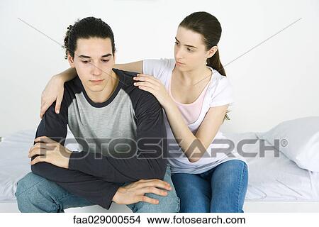 Young couple together on bed, female's arm around male's shoulder View Large Photo Image Picture - Young couple together on bed, female's arm around male's shoulder. Fotosearch