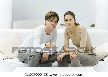 Young couple watching TV, pointing remote control at camera View Large Photo Image Stock Photo - Young couple watching TV, pointing remote control at camera. Fotosearch
