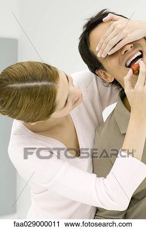 Young couple, woman holding hand over man's eyes, feeding him strawberry View Large Photo Image Stock Image - Young couple, woman holding hand over man's eyes, feeding him strawberry. Fotosearch