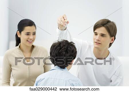 Stock Image - Young man and woman with boy, trying out head massager. Fotosearch