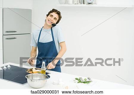 Young man cooking in kitchen, using cell phone View Large Photo Image Stock Image - Young man cooking in kitchen, using cell phone. Fotosearch