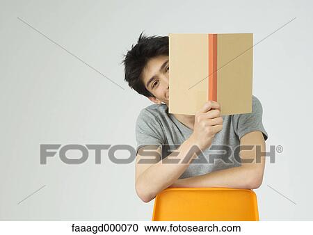 Young man holding up book, peeking around the edge of it View Large Photo Image Stock Image - Young man holding up book, peeking around the edge of it. Fotosearch