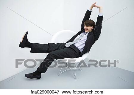 Young man in suit sitting in chair, legs outstretched, arms raised, full length View Large Photo Image Stock Photo - Young man in suit sitting in chair, legs outstretched, arms raised, full length. Fotosearch