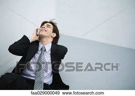 Young man in suit sitting on the ground, using cell phone, head back View Large Photo Image Stock Photo - Young man in suit sitting on the ground, using cell phone, head back. Fotosearch
