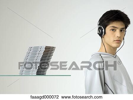 Stock Image - Young man listening to headphones, next to stack of cds. Fotosearch