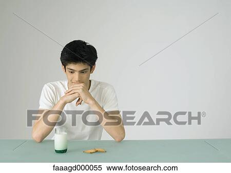 Stock Photography - Young man looking at glass of milk and cookies. Fotosearch